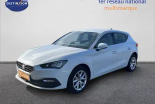 SEAT Leon blanc neige vue 3/4 avant droit, avec jantes alliage et calandre distinctive, stationnée sur sol gris.