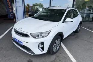 KIA Stonic blanc vue 3/4 avant droit, avec calandre noire et jantes alliage bicolores, stationné devant un bâtiment.