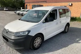 Volkswagen Caddy blanc Candy vu en 3/4 avant droit, avec pare-chocs noir mat et portes coulissantes.