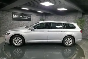 Volkswagen Passat SW gris métallisé vue de profil côté gauche dans un showroom avec mur en pierre grise.