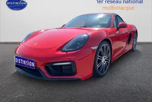 Vue 3/4 avant droite d'une Porsche Boxster rouge (981) avec jantes alu noires et becquet arrière visible.