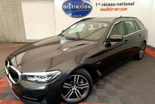 BMW Série 5 Touring 530e gris clair vue 3/4 avant droit, avec jantes alliage et phares LED allumés.