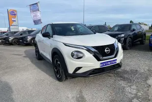 Nissan Juke blanc perle vu en 3/4 avant droit sur parking, avec calandre noire et jantes alliage noires.