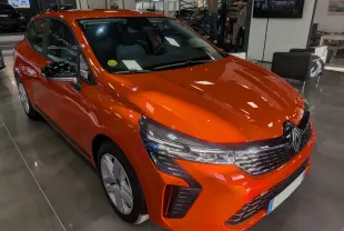 Renault Clio V Orange Valencia vue 3/4 avant droit en intérieur, avec calandre et phares LED distinctifs.