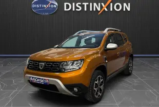 Dacia Duster orange en 3/4 avant droit, avec jantes bi-ton et rétroviseurs blancs, sur sol gris intérieur showroom.