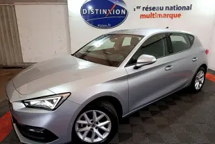 SEAT Leon gris foncé vue 3/4 avant droit dans un showroom avec éclairage intérieur et logo Distinxion en arrière-plan