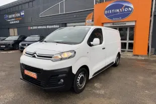 Citroën Jumpy blanc banquise en 3/4 avant droit, avec calandre noire et feux allumés, stationné devant un garage.