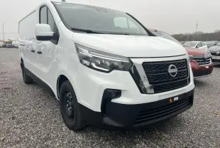 Vue 3/4 avant d’un utilitaire Nissan Primastar blanc avec calandre noire et jantes tôles noires sur un sol gravillonné.