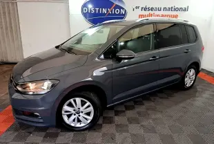 Vue 3/4 avant gauche d'un Volkswagen Touran gris foncé garé en intérieur avec jantes alliage et phares allumés.