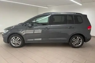 Profil côté gauche d'un Volkswagen Touran gris dauphin 2025 avec jantes alliage et lignes épurées dans un intérieur lumineux.