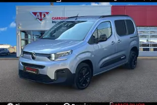 Vue 3/4 avant d'un Citroën Berlingo gris avec jantes noires, porte latérale coulissante droite visible, devant un garage.