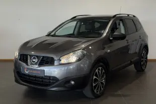 Nissan Qashqai+2 gris 2014 en 3/4 avant droit, avec jantes alliage et phares allumés en intérieur showroom.