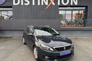 Peugeot 308 SW gris vue 3/4 avant droit, avec calandre chromée et toit ouvrant, devant un bâtiment Distinxion.