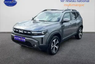 Dacia Duster gris schiste en 3/4 avant droit, avec jantes alu et barres de toit visibles.