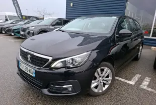 Peugeot 308 SW noire vue en 3/4 avant droit sous la pluie, avec jantes alliage et calandre chromée.