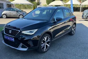 Vue 3/4 avant droite d'une SEAT Arona noire avec toit gris, jantes alliage 18'' et projecteurs LED allumés.
