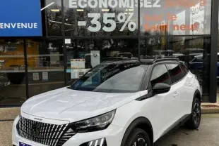 Vue 3/4 avant droite d'un Peugeot 2008 blanc avec toit noir et calandre distinctive, devant un concessionnaire multimarque.