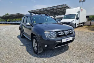Vue 3/4 avant d'un Dacia Duster gris foncé métal 2015, avec calandre distinctive et barres de toit visibles.