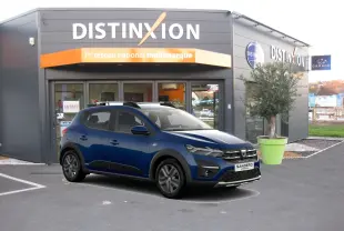 Dacia Sandero Stepway bleu vue 3/4 avant droit, avec toit noir et détails noirs contrastants, devant un garage Distinxion.