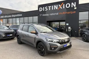 Vue 3/4 avant du Dacia Jogger gris schiste métal avec calandre noire et jantes aluminium noires devant un showroom Distinxion.