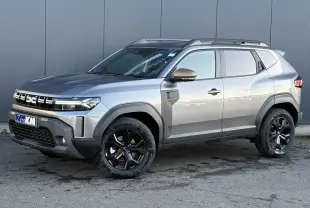 Vue 3/4 avant droit du Dacia Duster 2026 gris schiste avec jantes noires et barres de toit longitudinales.