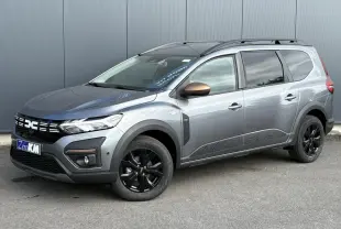 Dacia Jogger Gris Schiste en 3/4 avant droit, avec jantes noires et barres de toit longitudinales.