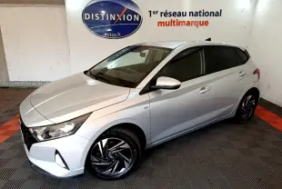 Vue 3/4 avant droite d'une Hyundai i20 gris clair 2022 avec jantes noires et vitres teintées en intérieur showroom.