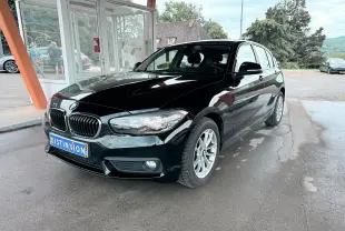 BMW Série 1 noire vue en 3/4 avant droit, avec calandre caractéristique et jantes argentées sous un abri.