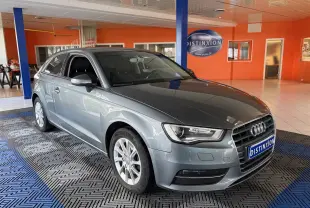 Audi A3 gris vue 3/4 avant droit, avec calandre distinctive et jantes alliage, en intérieur showroom.