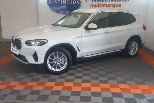 BMW X3 xDrive30e blanc en vue 3/4 avant droit, avec phares LED allumés et jantes alliage visibles.