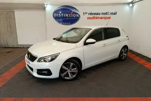 Peugeot 308 blanc vue 3/4 avant droit dans un showroom avec jantes alliage et phares allumés.