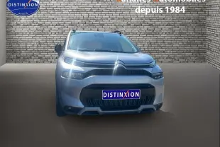 Vue frontale d'un Citroën C3 Aircross gris foncé avec projecteurs allumés, sur fond de mur en briques.
