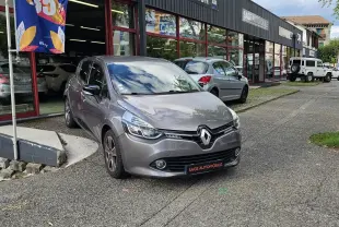 Renault Clio IV grise vue 3/4 avant droit, garée devant un garage avec plaque SAGE AUTOMOBILE.