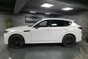 Vue de profil côté gauche du Mazda CX-60 blanc Arctic White avec jantes alliage noires dans un showroom.