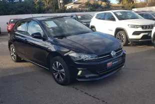 Volkswagen Polo noire vue en 3/4 avant droit avec jantes alliage et feux diurnes allumés sur parking.