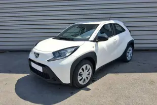 Toyota Aygo X blanc pur vue 3/4 avant droit, avec protections noires autour des roues et rétroviseurs noirs.