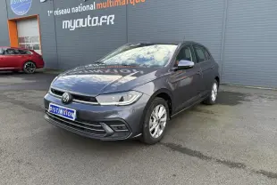 Volkswagen Polo gris cendre vue 3/4 avant droit, stationnée devant un mur gris avec logo Distinxion.