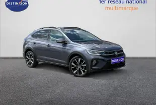 Volkswagen Taigo gris Ascot en vue 3/4 avant droit, avec jantes alliage et barres de toit visibles.