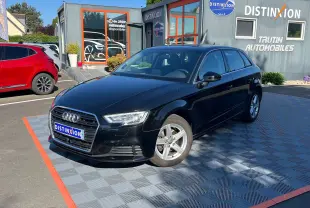 Audi A3 Sportback noir métal vue 3/4 avant droit, stationnée devant un showroom Distinxion par temps ensoleillé.