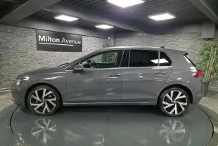 Profil côté gauche d'une Volkswagen Golf gris Urano avec jantes alliage 18 pouces dans un showroom intérieur.