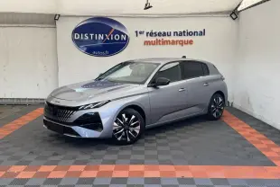 Peugeot 308 gris clair vue 3/4 avant droit, avec calandre distinctive et jantes noires et argentées.