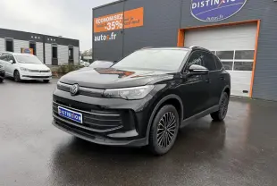 Volkswagen Tiguan noir grenadille métallisé vu en 3/4 avant droit sur parking devant un bâtiment commercial.