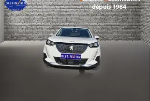 Vue frontale d'un Peugeot 2008 blanc 2020 avec calandre noire et phares LED, sur fond de mur en briques grises.