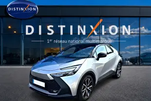 Toyota C-HR 1.8 hybride gris en 3/4 avant droit, avec toit noir et jantes alliage visibles devant un showroom Distinxion.