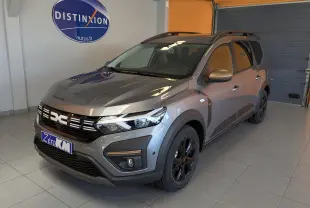 Vue 3/4 avant droite d'un Dacia Jogger gris schiste métallisé avec jantes noires et toit ouvrant en intérieur showroom.