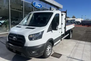 Vue 3/4 avant droit d’un Ford Transit Chassis Cabine blanc avec benne et coffre, roues jumelées, stationné devant un showroom Ford.