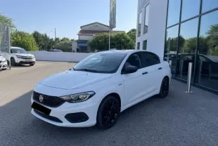 Vue 3/4 avant droite d'une Fiat Tipo blanche 2019 avec jantes noires, garée devant un bâtiment vitré.
