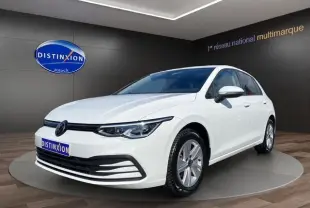 Vue 3/4 avant d'une Volkswagen Golf VIII blanche avec vitres surteintées, en présentation dans un showroom.