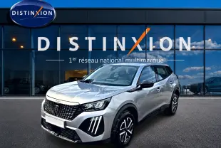 Peugeot 2008 gris en 3/4 avant droit, avec calandre noire et feux LED distinctifs, devant showroom Distinxion.