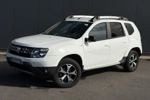 Dacia Duster blanc glacier en 3/4 avant droit avec barres de toit alu et jantes diamantées noires.